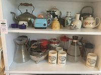 Shelf view with assortment of tea pots, honey pot, Bodum carafes, mugs and decorative vases.