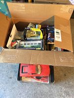 Cardboard box with multiple boxed die-cast vehicles and a loose red Ferrari F40 model at bottom