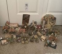 Full view of multiple David Winter Cottage miniature figurines arranged on floor including some paper documentation and a circular decorative plate.