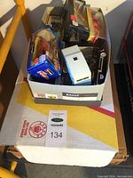 Box containing boxed die-cast vehicles and loose trailer on top of cardboard boxes