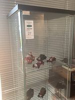 Full view of the tall glass display case containing multiple diecast cars on shelves, one with a driver figure as a bank.