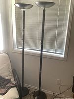 Two black metal base floor lamps shown full height in front of window blinds.