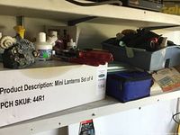 Shelf with a box labeled Mini Lanterns Set of 4, blue pouch, and tools on gray tray.