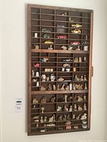 Full view of antique wooden ink drawer shelf mounted on wall with assorted miniatures displayed in compartments.