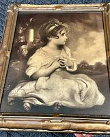 Framed sepia-tone art print of a young girl sitting, detailed with shadows and soft focus. The girl wears a flowing dress and a headband, holding an object, probably a cup.