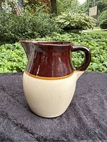 Full front view of two-tone brown and cream stoneware pitcher showing the spout and opening.