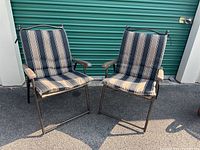 Two folding lawn chairs with striped padded cushions in front of a green storage unit door.