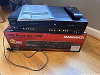 DVD Recorder/VCR combo unit on top of the original product box, showing front panel buttons and remote control resting on top.