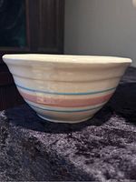 Side view of off-white ceramic mixing bowl with pink and blue bands around exterior, showing shape and glazing.
