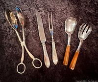 Full set of utensils including salad scissors, carving knife and fork, and Lucite handled salad servers on dark fabric.