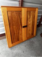 Closed front view of the large shallow oak wall cabinet showing the wood grain, rectangular frame, two paneled doors and a central handle.