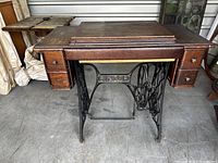 Front view of Singer treadle sewing machine cabinet showing oak wood cabinet body and cast iron base with Singer logo