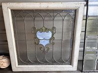 Square stained glass window panel in white wooden frame with central decorative motif photographed front on.