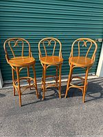 Three vintage bentwood bar stools, all with wooden seats and classic scroll back design, shown outdoors against a green door.