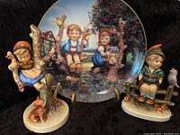 Photo of the Danbury Mint collectors plate in front of two Goebel Hummel figurines, showing detailed painted scene of children and nature animals, including fox and birds.