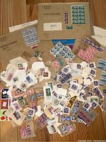 Overview of numerous vintage stamps and postal pieces scattered on wood surface, showing a variety of colors, denominations and postmarks.