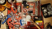 Overview of assorted tools on a red surface including flashlights, wrenches, hammers, hardware boxes, and miscellaneous small items