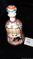 Photo of ceramic saki bottle decanter showing front panel with seated figure and floral decorative elements.