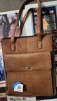 Brown leather messenger bag shown upright to display front flap pocket and two shoulder straps