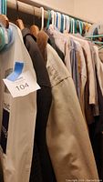 Men's coats, jackets, shirts, and pants hanging on hangers in a closet, showing a range of neutral colors and styles.