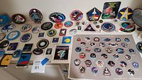 Photo showing a wide assortment of NASA mission souvenir buttons, pins, patches, and stickers, arranged flat on a surface