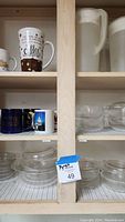 Wooden shelf displaying stacked clear Pyrex glass bowls with lids on lower shelves and coffee cups on upper shelves.