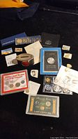 Overview of chrome bank, coin sets, silver dollar, stamps and bookmark