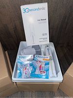 Five boxed 30 Second Smile electric toothbrushes with one open box showing contents: toothbrush handle, user manual, replacement heads.