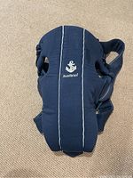 Front view of navy blue Baby Bjorn baby carrier with anchor embroidery and white piping detail.