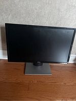 View of Dell 24-inch widescreen LED monitor with black bezel and silver base on a wooden floor.