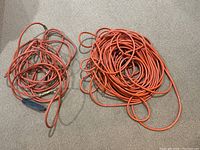 Photo of two orange electrical extension cords, one longer and one shorter, on carpeted floor