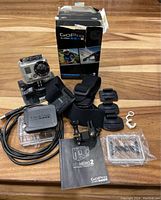 Full laid out view of GoPro HERO2 camera, original box, straps, mounts, USB cable, frame, and manual.