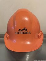 Front view of orange hard hat with Hermès horse-and-carriage logo