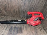 Side view of the red and black Homelite electric leaf blower with the nozzle facing left on a wooden surface.