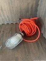 Photo of portable work light with orange extension cord coiled behind it on wood background.