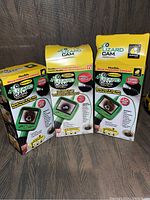 Three boxed Lizard Cam micro-inspection cameras displayed upright on a wooden floor. Boxes are yellow with green and black imagery of the device and its flexible probe camera.