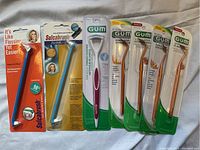 Dental tools lot including Sulcabrush, GUM tongue cleaner and gum stimulators all sealed in retail packaging on a cloth background.