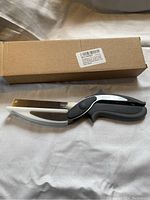 Closed view of Chopeasy food chopper with black and gray handle, stainless steel curved blade, and original cardboard box.