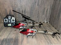 Two red and silver Protocol P Series remote control helicopters alongside a black Protocol remote control on a wood textured surface.