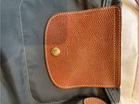 Close-up of brown leather flap with gold snap button on the bag showing material and stitching details.