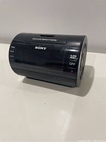 Front angle view of black Sony Dream Machine alarm clock with display and controls visible, showing snooze/brightness button on top and alarm off/reset switch on side.