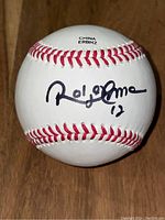 Close-up of signed baseball showing Roberto Alomar autograph with number 12 on white ball with red stitching.