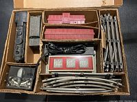 Photo of open storage box showing black locomotive, red railroad cars, Union Station building, transformer, and metal track pieces in sections.