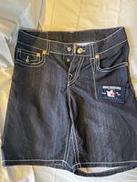 Front view of dark blue True Religion swim trunks showing white contrast stitching and patch pocket with branding.