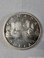 Front side of 1965 Canada silver dollar coin showing canoe paddling design, year, and denomination.