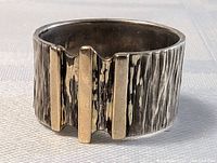 Close-up of sterling silver ring face showing hammered texture and three vertical 14K gold bars on band