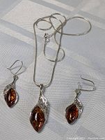 Sterling silver amber necklace with matching earrings laid out on fabric, showing the detailed leaf-shaped design encasing the amber stones.