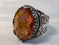 Close-up side angle view of vintage sterling silver ring showcasing ornate filigree band and large oval faceted pinkish orange stone.