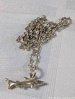 Close-up of the shark pendant with chain lying on a fabric surface showing the detail and texture of the silver pendant and chain.