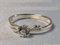 Close-up photo of sterling silver ring with clear round quartz stone in six prong setting, visible band design and markings inside the band.